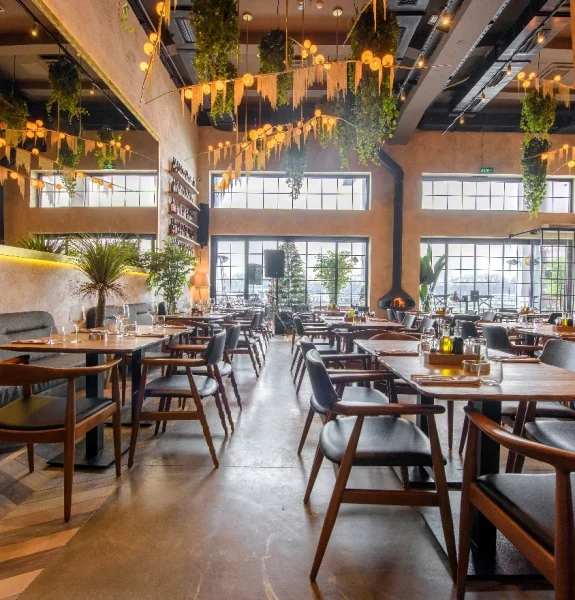 En välkomnande restaurang med specialbyggda träbord och -stolar, mässingsdetaljer och växter som ger en naturlig och varm känsla till inredningen. Restaurangsinredning Göteborg.